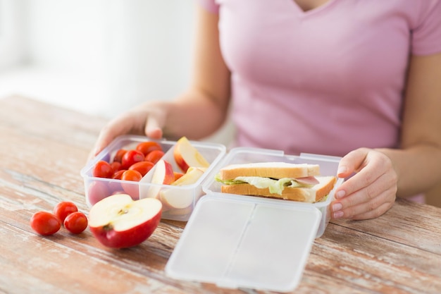 healthy eating, storage, dieting and people concept - close up of woman with food in plastic container at home kitchen