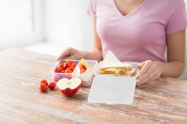 healthy eating, storage, dieting and people concept - close up of woman with food in plastic container at home kitchen