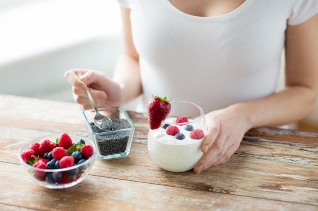 healthy eating, vegetarian food, diet and people concept - close up of woman hands with yogurt, berries and poppy or chia seeds on spoon