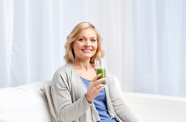 healthy eating, vegetarian food, dieting, detox and people concept - smiling middle aged woman drinking green fresh vegetable juice or smoothie from glass at home