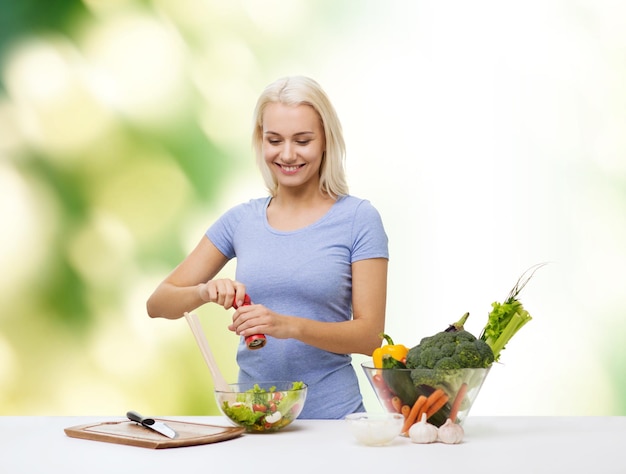 healthy eating, vegetarian food, dieting and people concept - smiling young woman cooking vegetable salad over green natural background