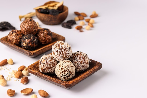 Healthy energy balls of nuts oatmeals and dried fruit with coconut flax and sesame seeds on wooden coconut plates on a white background horizontal orientation copy space