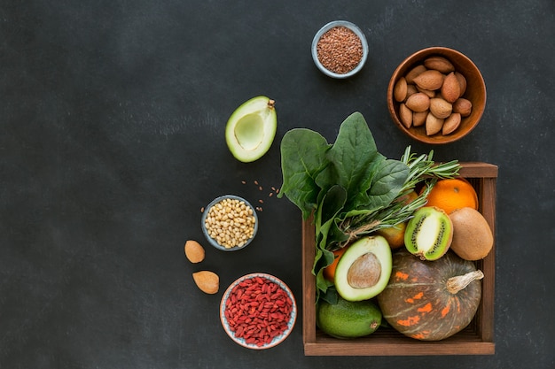 Healthy farmer organic food in wooden box: fruit, vegetables, seeds, superfood, leaf vegetable on black background. Clean eating selection concept