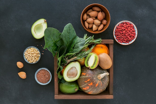 Healthy farmer organic food in wooden box: fruit, vegetables, seeds, superfood, leaf vegetable on black background. Clean eating selection concept