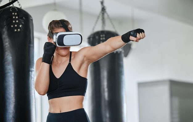 Healthy fit and active boxing woman with a VR headset to access the metaverse while exercising training and working out in a gym Female boxer doing a workout in virtual reality with technology