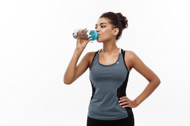 Healthy and Fitness concept beautiful African American girl in sport clothes drinking water after workout Isolated on white studio background