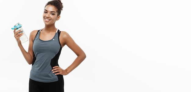 Healthy and Fitness concept beautiful African American girl in sport clothes holding water bottle after workout Isolated on white studio background