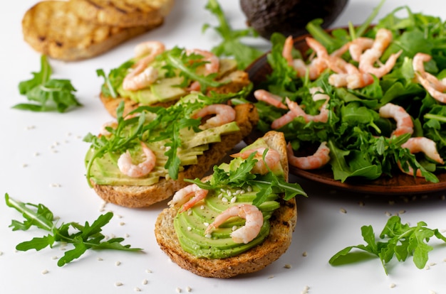 Healthy fitness food. Toasts with avocado, shrimps and arugula salad on white background