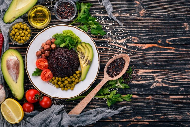 Healthy food Black rice avocado cherry tomatoes green peas and hazelnut On a wooden background Top view Free space for your text