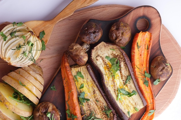 Healthy food closeup Baked slices of eggplant beets carrots onions potatoes whole mushrooms spices and herbs on a wooden board on a white background