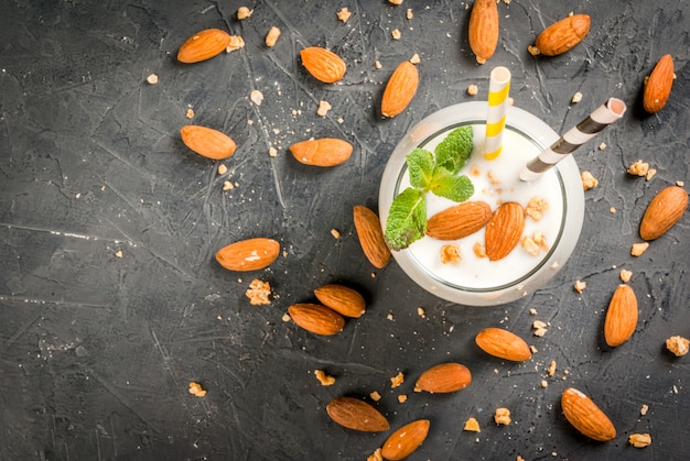 Healthy food. Dietary breakfast or snack. White smoothies made from yogurt, banana and almond nuts. decorated with mint. On a dark concrete table with ingredients, striped straws.  top view