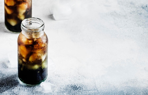 Healthy food and drink concept cold black detox mineral water with crushed ice in glass bottles with activated charcoal gray stone table background trendy beverage copy space selective focus