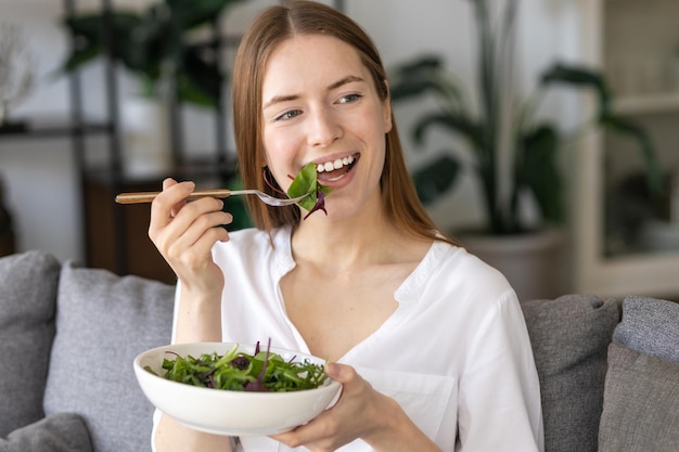 Healthy food lifestyle concept. Beautiful young woman with plate of fresh green salad at home