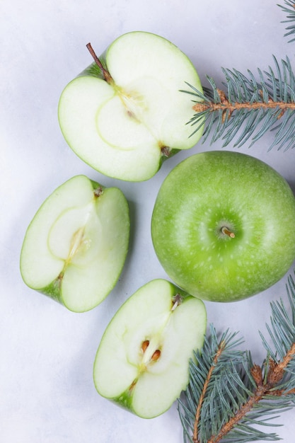 Healthy food and lifestyle concept Green ripe juicy apple and apple pieces with fir branches on a light background Closeup