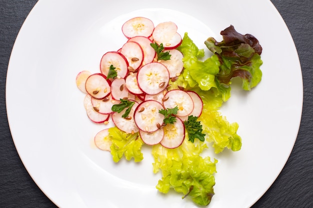 Healthy food organic slices radish salad in white plate on black slate board