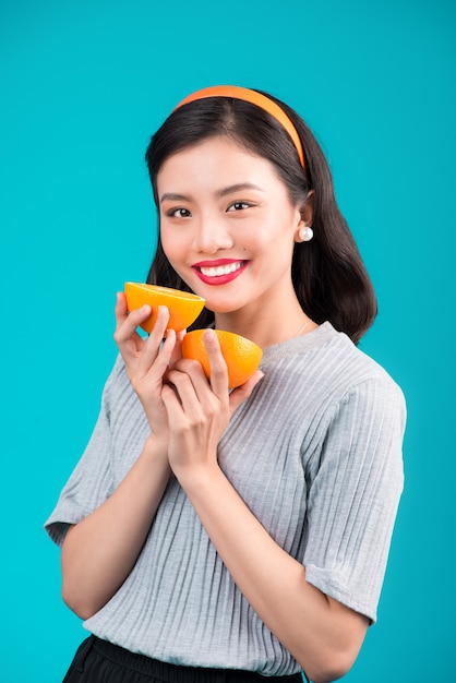 Healthy food. Smiling lovely pinup asian girl holding orange over blue background.