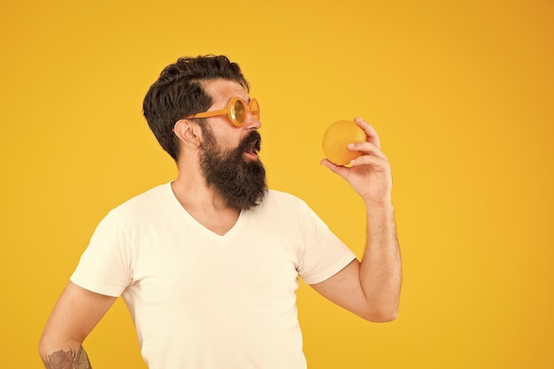 Healthy food taste better Surprised hipster looking at healthy orange fruit on yellow background Bearded man with healthy vitamin snack Eat healthy be nutrition wealthy