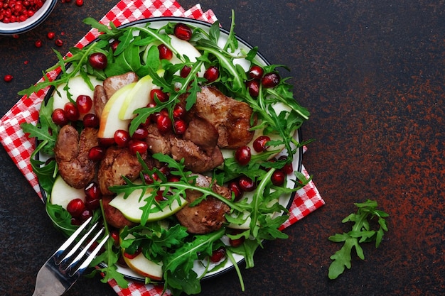 Healthy fresh chicken liver salad with apple pomegranate and arugula Brown kitchen table background top view copy space