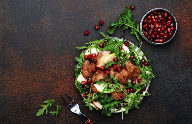 Healthy fresh chicken liver salad with apple pomegranate and arugula Brown kitchen table background top view copy space