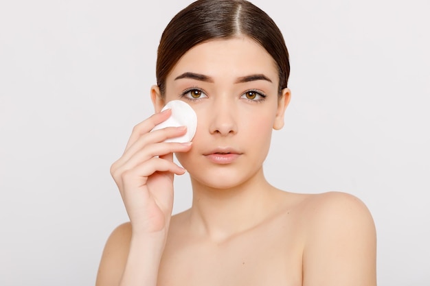 Healthy fresh girl removing makeup from her face with cotton pad Beauty woman cleaning her face with cotton swab pad isolated on grey background Skin care and beauty concept