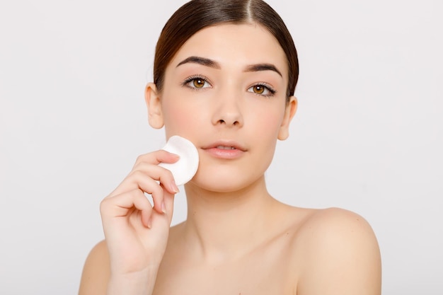 Healthy fresh girl removing makeup from her face with cotton pad Beauty woman cleaning her face with cotton swab pad isolated on grey background Skin care and beauty concept