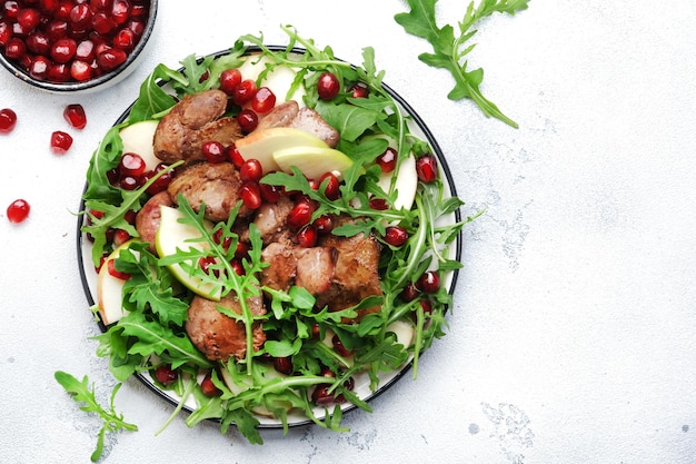 Healthy fresh salad with chicken liver apple pomegranate and arugula White kitchen table background top view