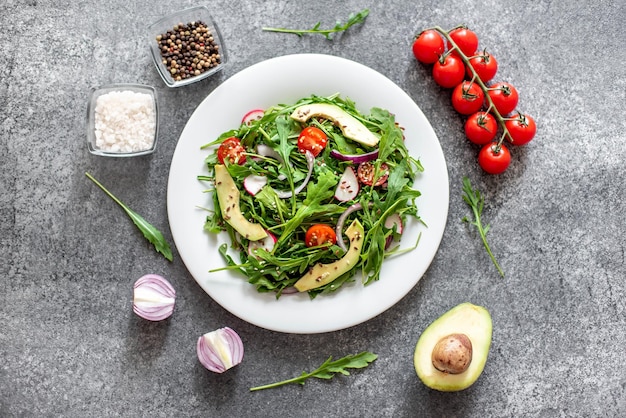 Healthy fresh vegetable salad tomatoes arugula avocado radish on a stone background