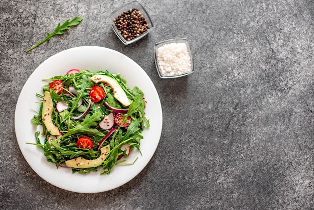 Healthy fresh vegetable salad tomatoes arugula avocado radish on a stone background