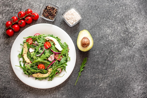 Healthy fresh vegetable salad tomatoes arugula avocado radish on a stone background