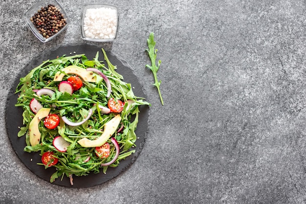 Healthy fresh vegetable salad tomatoes arugula avocado radish on a stone background