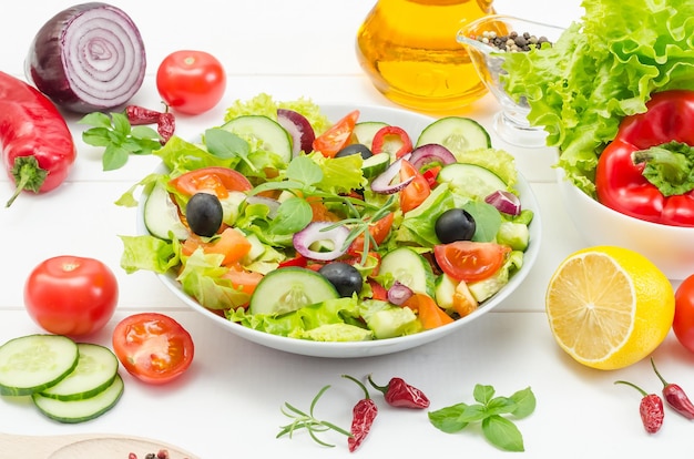 Healthy fresh vegetable salad with tomatoes, cucumbers and bell peppers in a plate on a white wooden background.