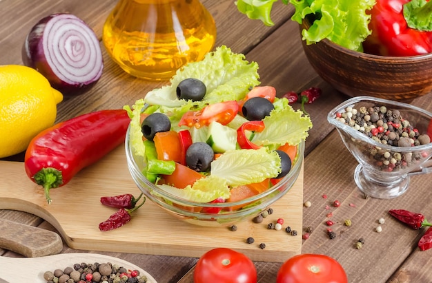 Healthy fresh vegetable salad with tomatoes, cucumbers and olives in a plate on a dark wooden background.