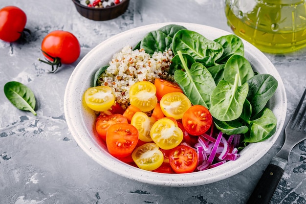 Healthy green bowl salad with spinach quinoa yellow and red tomatoes onions and seeds on gray background