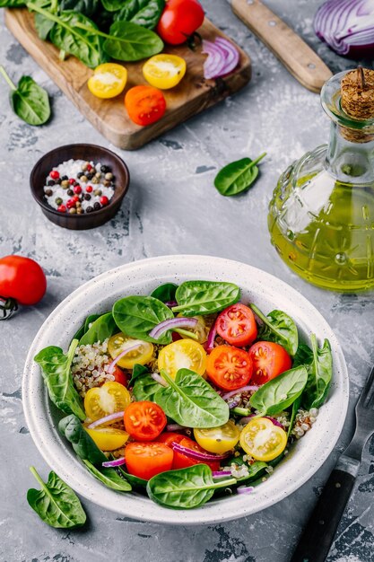 Healthy green bowl salad with spinach quinoa yellow and red tomatoes onions and seeds on gray background