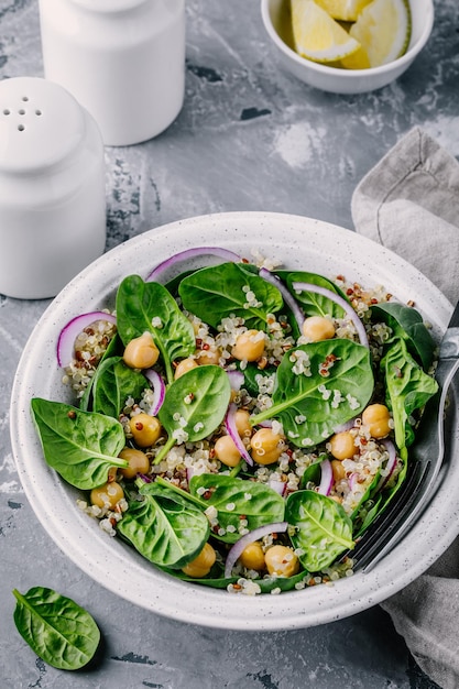 Healthy green salad bowl with spinach quinoa chickpeas and red onions on gray background