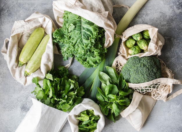 Healthy green vegan ingredients for cooking. Various clean green vegetables and herbs in textile bags. Products from the market without plastic. Zero waste concept flat lay. 