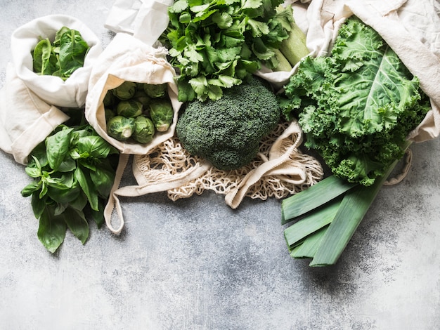 Healthy green vegan ingredients for cooking. Various clean green vegetables and herbs in textile bags. Products from the market without plastic. Zero waste concept flat lay. 