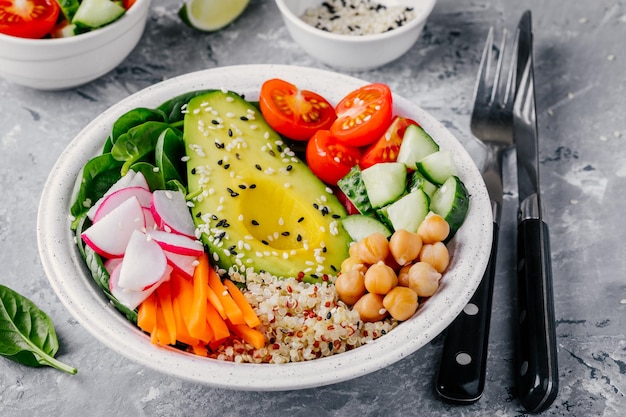 Healthy green vegetarian buddha bowl salad with vegetables and quinoa spinach avocado cucumbers tomatoes carrots radishes chickpeas with sesame seeds