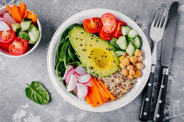 Healthy green vegetarian buddha bowl salad with vegetables and quinoa spinach avocado cucumbers tomatoes carrots radishes chickpeas with sesame seeds