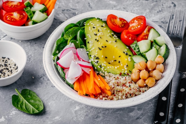 Healthy green vegetarian buddha bowl salad with vegetables and quinoa spinach avocado cucumbers tomatoes carrots radishes chickpeas with sesame seeds