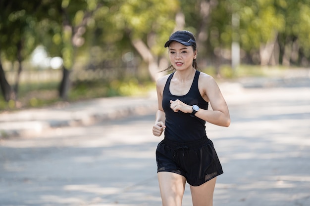 A healthy happy Asian woman runner in black sport outfits jogging in the natural city park under evening sunset