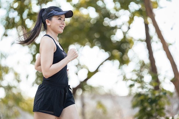 A healthy happy Asian woman runner in black sport outfits jogging in the natural city park under evening sunset