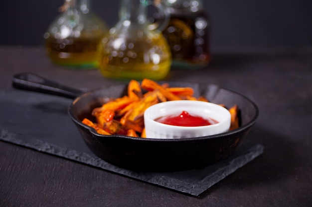 Healthy homemade baked sweet potato fries on the metal pan with dip tomatoes sauce.