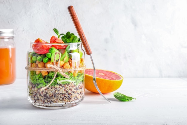 Healthy homemade salad in glass jar with quinoa, vegetables and herbs om white background. Vegan food concept.