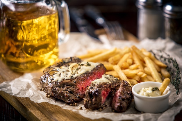 Healthy lean grilled medium-rare steak with french fries, and beer, and a spice in a rustic pub or tavern. Food-styling