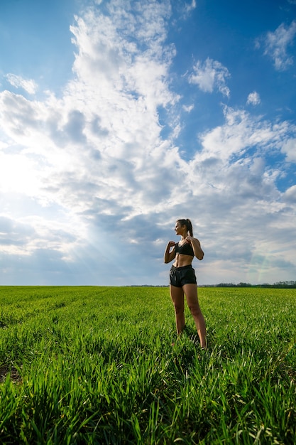 Healthy lifestyle concept. Young attractive woman in sportswear does stretching her hand before training on the nature against a blue sky. Muscle warming