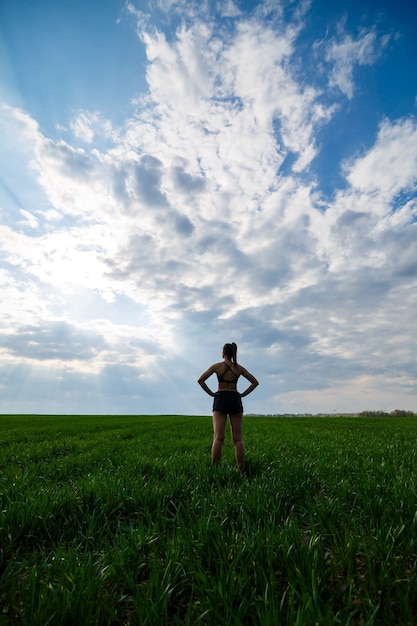 Healthy lifestyle concept. Young attractive woman in sportswear does stretching her hand before training on the nature against a blue sky. Muscle warming