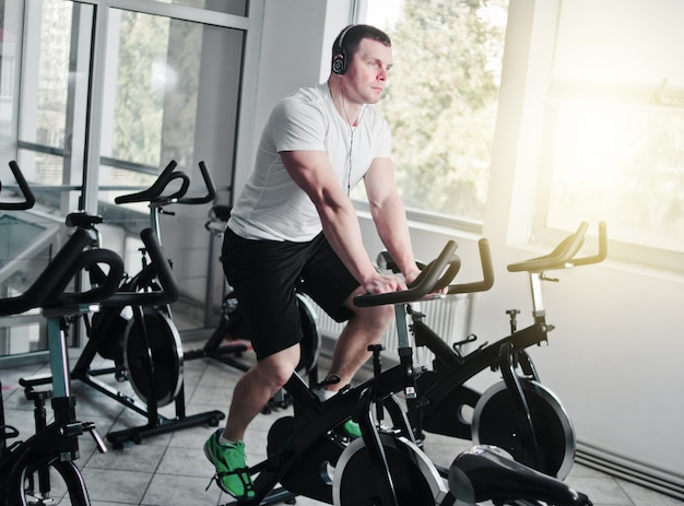 Healthy lifestyle concept. Young sporty man in white t-shirt and shorts is exercising bike at spinning class . Cardio training