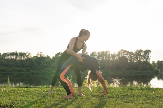 Healthy lifestyle and people concept - Flexible women doing yoga in the summer park