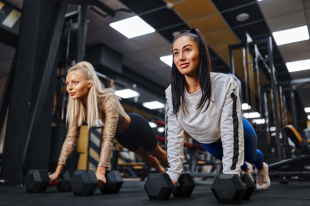 Healthy lifestyle portrait of two young athletic girls doing plank in the gym